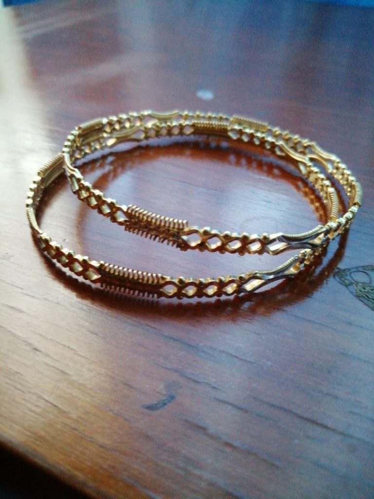 A pair of gold bracelets sitting on top of a wooden table.