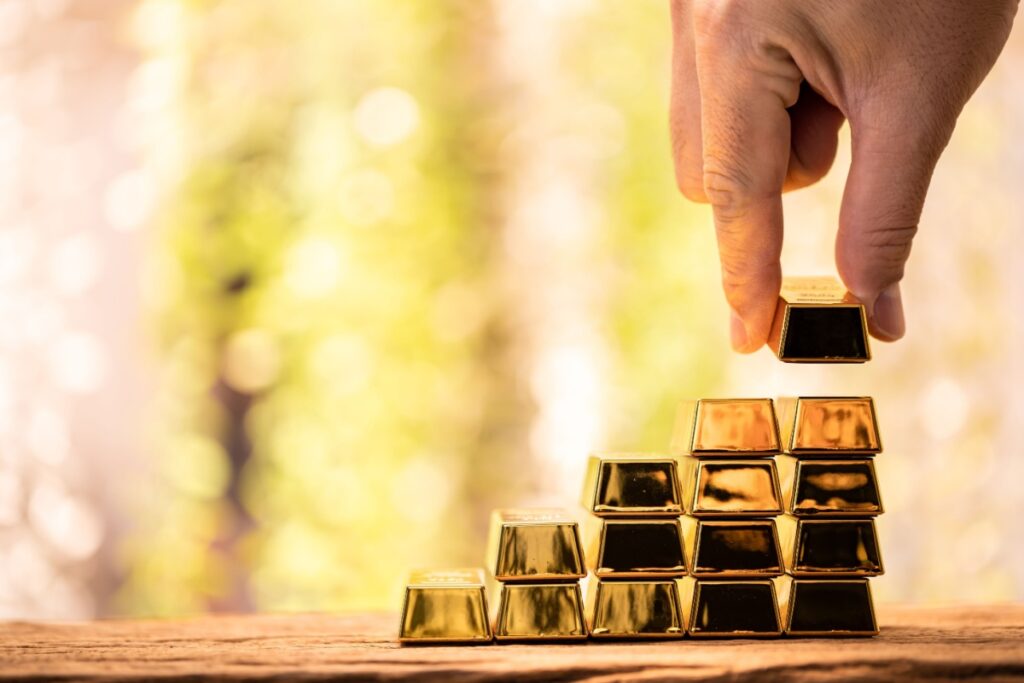A hand is holding onto gold bars as they are stacked on top of each other.